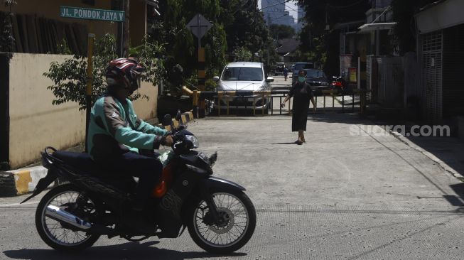 Warga melintas di depan portal saat diberlakukannya penutupan akses wilayah di Komplek Pondok Jaya, Mampang Prapatan, Jakarta Selatan, Selasa (31/1). [Suara.com/Angga Budhiyanto]