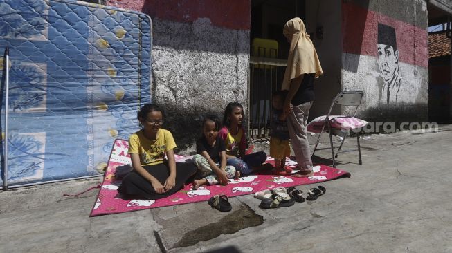 Warga bersama keluarga berjemur di bawah sinar matahari pagi di Gang Haji Sairan, Kelurahan Jati Padang, Pasar Minggu, Jakarta Selatan, Selasa (31/1). [Suara.com/Angga Budhiyanto]