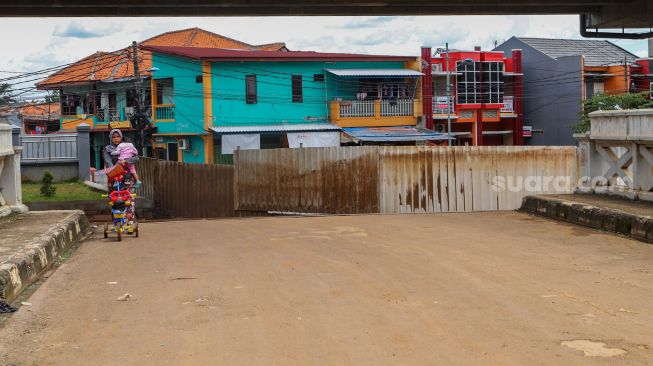 Warga melintasi jalan yang ditutup dengan seng untuk meminimalisir penyeberan  Corona di kawasan sekitar, Jakarta Timur, Selasa (31/3). [Suara.com/Alfian Winanto]