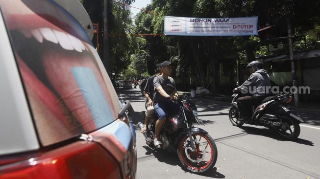 Pengendara sepeda motor melintas di bawah spanduk penutupan akses wilayah di Komplek Pondok Jaya, Mampang Prapatan, Jakarta Selatan, Selasa (31/1). [Suara.com/Angga Budhiyanto]
