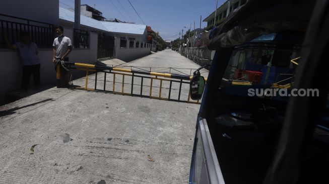 Warga berdiri di depan portal saat diberlakukannya penutupan akses wilayah di Komplek Pondok Jaya, Mampang Prapatan, Jakarta Selatan, Selasa (31/1). [Suara.com/Angga Budhiyanto]