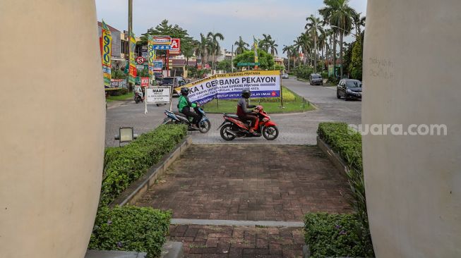 Pengendara motor melintas di depan spanduk pengumuman berisi karantina wilayah perumahan elit Kemang Pratama, Bekasi, Jawa Barat, Rabu (1/4). [Suara.com/Alfian Winanto]