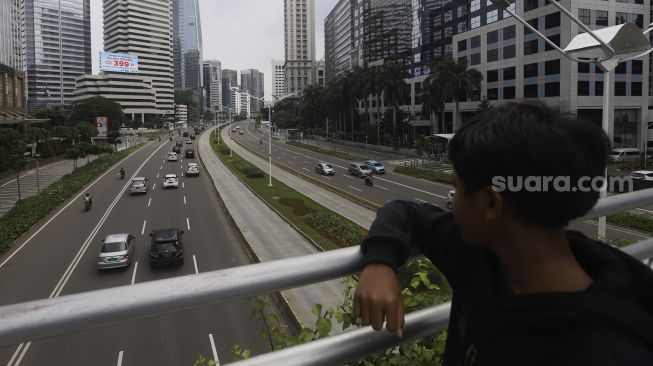 Seorang anak mengamati kendaraan yang melintas di Jalan Jendral Sudirman, Jakarta, Rabu (1/4). [Suara.com/Angga Budhiyanto]