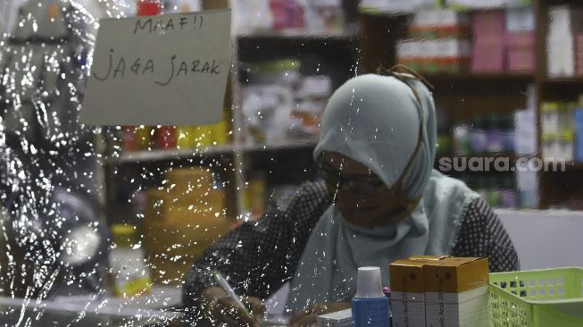 Pekerja menulis resep dari balik plastik pembatas di salah satu apotek di kawasan Pasar Baru, Jakarta, Jumat (3/4). [Suara.com/Angga Budhiyanto]