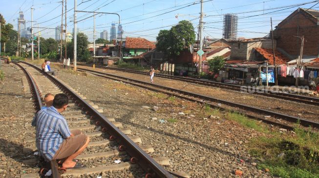 Warga bersama anaknya berjemur di rel kereta api di kawasan Menteng, Jakarta, Jumat (3/4). [Suara.com/Oke Atmaja]
