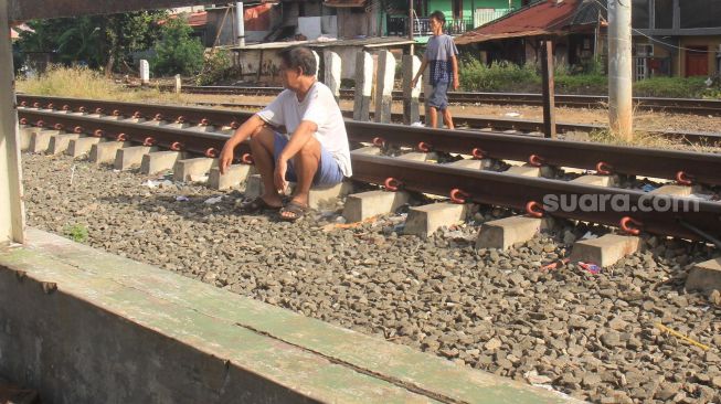 Warga berjemur duduk di rel kereta api di kawasan Menteng, Jakarta, Jumat (3/4). [Suara.com/Oke Atmaja]