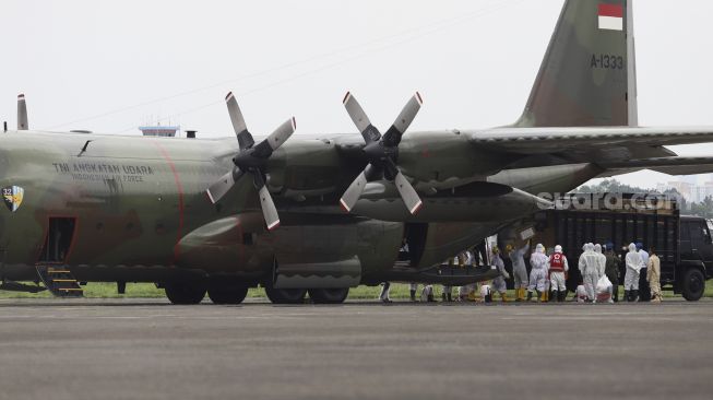 Petugas Palang Merah Indonesia (PMI) menyemprotkan cairan disinfektan kepada petugas yang akan memindahkan logistik kesehatan dari pesawat Hercules C-130 di Landasan Udara (Lanud) Halim Perdanakusuma, Jakarta, Senin (23/3). [Suara.com/Angga Budhiyanto]