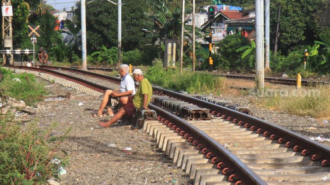 Dua orang warga berjemur di rel kereta api di kawasan Menteng, Jakarta, Jumat (3/4). [Suara.com/Oke Atmaja]