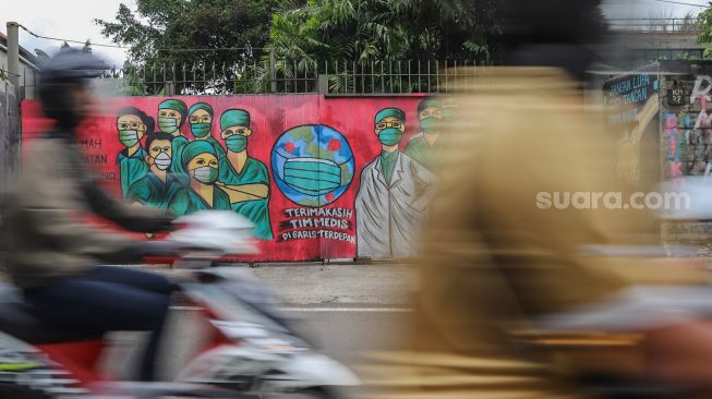 Kendaraan melintas didepan mural bertemakan tentang virus Corona dengan gambar para tenaga medis di Jalan Raya Bogor,  Depok, Jawa Barat, Senin (6/4).   [Suara.com/Alfian Winanto]
