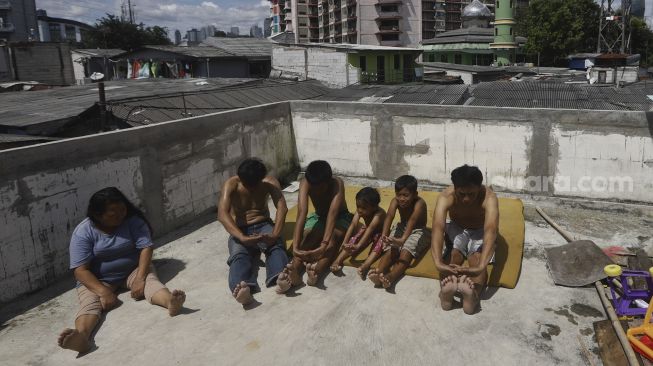 Warga berjemur sambil melakukan olahraga kecil di balkon rumahnya di permukiman padat di kawasan Pejompongan, Jakarta, Selasa (7/4). [Suara.com/Angga Budhiyanto]