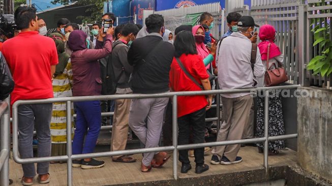 Sejumlah warga mengantri didepan gerbang pabrik di Jalan Raya Bogor, Depok, Jawa Barat, Selasa (7/4). [Suara.com/Alfian Winanto]