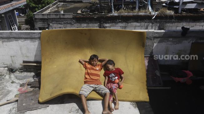 Dua orang bocah berjemur di balkon rumahnya di permukiman padat di kawasan Pejompongan, Jakarta, Selasa (7/4). [Suara.com/Angga Budhiyanto]