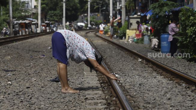 Warga berjemur sambil melakukan olahraga di bantaran rel di kawasan Pejompongan, Jakarta, Selasa (7/4). [Suara.com/Angga Budhiyanto]
