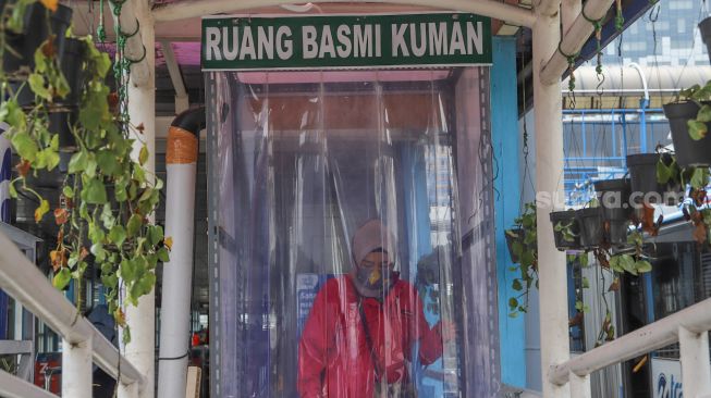 Penumpang bus Transjakarta membersihkan diri didalam ruang disinfektan yang disediakan oleh pihak Transjakarta di Halte Transjakarta Harmoni, Jakarta, Rabu (8/4).  [Suara.com/Alfian Winanto]
