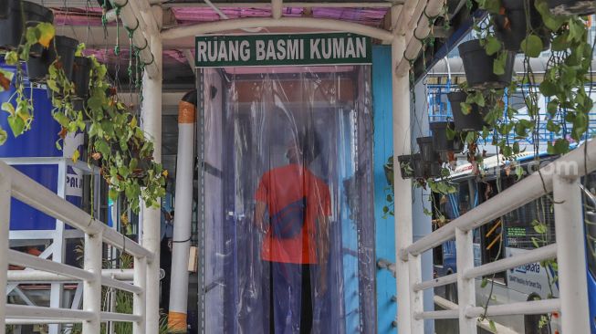 Penumpang di dalam  bilik disinfektan untuk masuk ke Halte Transjakarta Harmoni, Jakarta, Rabu (8/4). [Suara.com/Alfian Winanto]