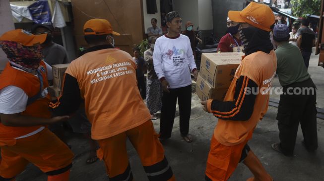 Petugas membawa sembako dan makanan siap saji dari truk di Kelurahan Kebon Baru, Tebet, Jakarta Selatan, Rabu (8/4). [Suara.com/Angga Budhiyanto]