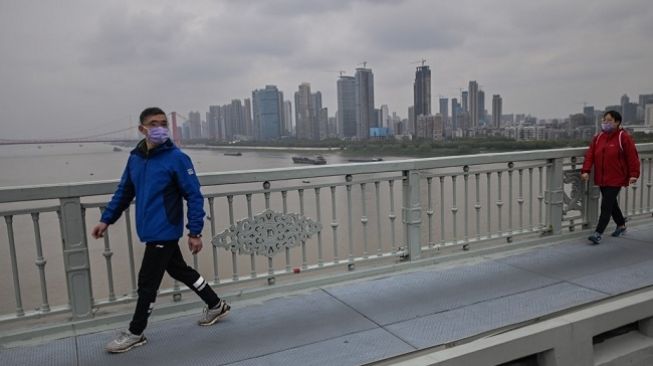 Pejalan kaki melintas di trotoar Kota Wuhan selama masa lockdown karena virus corona. (Foto: AFP)