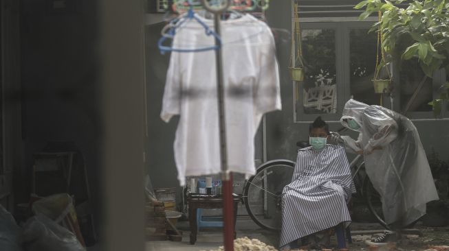 Seorang tukang cukur menggunakan Alat Pelindung Diri (APD) ketika memotong rambut di halaman rumah pelanggan di Pekanbaru, Riau, Kamis (9/4). [ANTARA FOTO/Rony Muharrman]