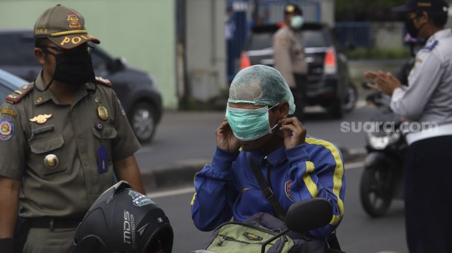 Polisi lalulintas beserta Dinas Perhubungan (Dishub) memeriksa pengendara sepeda motor saat melaksanakan pengawasan dalam penerapan Pembatasan Sosial Berskala Besar (PSBB) di jalan perbatasan Depok-Jakarta, Jumat (10/4). [Suara.com/Angga Budhiyanto]