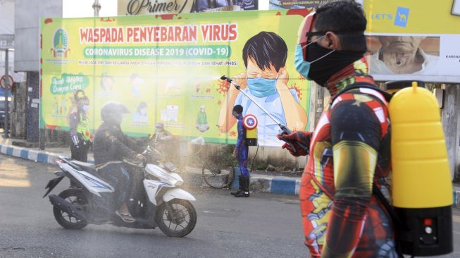 Sejumlah petugas kepolisian berpakaian superhero menyemprotkan cairan disinfektan di Jalan Panglima Sudirman kawasan Kebonagung, Pasuruan, Jawa Timur, Kamis (9/4). [ANTARA FOTO/Umarul Faruq]