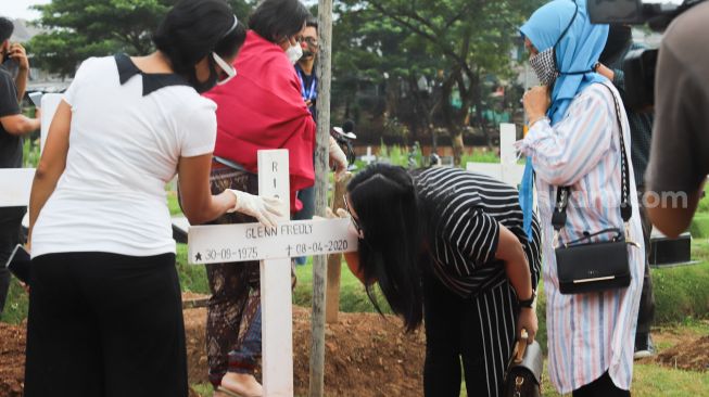 Mutia Ayu mencium nisan Glenn Fredly usai berziarah di TPU Tanah Kusir, Jakarta Selatan, Minggu (12/4). [Suara.com/Alfian Winanto]