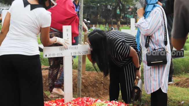 Mutia Ayu mencium nisan Glenn Fredly usai berziarah di TPU Tanah Kusir, Jakarta Selatan, Minggu (12/4). [Suara.com/Alfian Winanto]