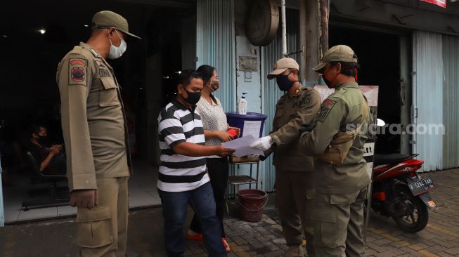 Petugas Satpol PP memberikan surat himbauan kepada pelaku usaha kecil di Kramat Jati, Jakarta Timur, (13/4). [Suara.com/Alfian Winanto]
