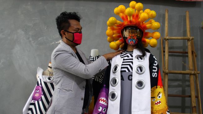 Perancang busana Agus Sunandar (kiri) memakaikan busana karyanya yang berjudul Covid Dua Puluh kepada seorang model di sebuah studio di Malang, Jawa Timur, Selasa (14/4). [ANTARA FOTO/Ari Bowo Sucipto]