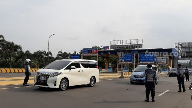 Petugas memberhentikan sejumlah mobil di Exit Tol Bekasi Barat saat PSBB. (Suara.com/Ummi Saleh)