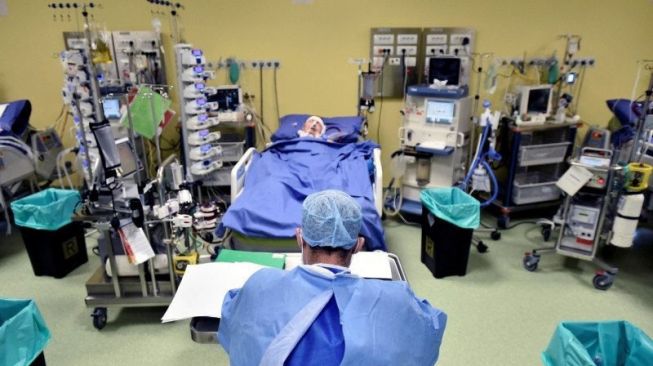 Seorang staf medis dengan pakaian pelindung terlihat di depan seorang pasien dengan penyakit virus Corona Covid-19 di dalam sebuah unit perawatan intensif (ICU) di rumah sakit San Raffaele, Milan, Italia, Jumat (27/3/2020). [Antara/Reuters/Flavio Loscalzo]