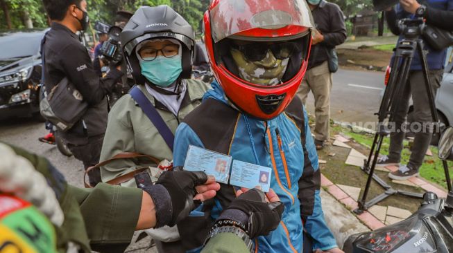 Petugas mencocokan KTP pengendara yang berboncengan saat Pemberlakuan PSBB di Check Point PSBB Kota Depok dibawah Flyover UI, Lenteng Agung, Jakarta Selatan, Rabu (15/4). [Suara.com/Alfian Winanto]