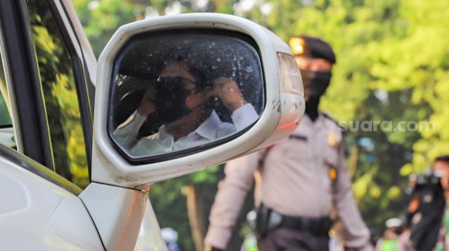 Pengendara mobil bergegas mengenakan masker saat dihentikan petugas di Check Point PSBB Kota Depok dibawah Flyover UI, Lenteng Agung, Jakarta Selatan, Rabu (15/4). [Suara.com/Alfian Winanto]