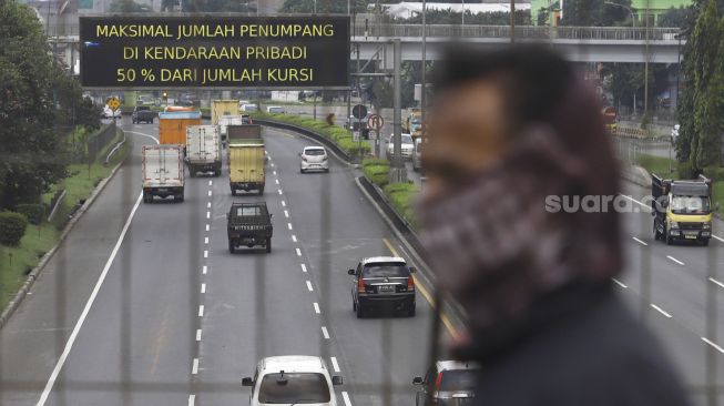 Kendaraan melintas di bawah videotron imbauan peraturan penerapan Pembatasan Sosial Berskala Besar (PSBB) di ruas tol Jor di kawasan Pasar Rebo, Jakarta, Kamis (16/4). [Suara.com/Angga Budhiyanto]