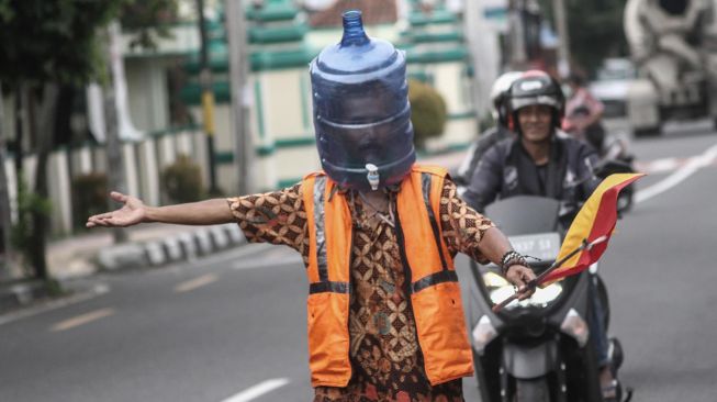 Ali Akbar (52) Sukarelawan Pengatur Lalu Lintas (Supeltas) mengatur lalu lintas mengenakan pelindung wajah dari galon bekas di Jalan Tamansiswa, DI Yogyakarta, Rabu (15/4). Ali Akbar menggunakan pelindung wajah unik itu saat mengatur lalu lintas guna mengantisipasi penularan virus Corona COVID-19.  [ANTARA FOTO/Hendra Nurdiyansyah]