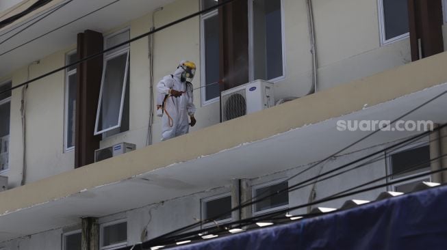 Petugas Palang Merah Indonesia (PMI) menyemprotkan cairan disinfektan di lingkungan asrama Sekolah Tinggi Teknologi (STT) Bethel di kawasan Petamburan, Jakarta, Jumat (17/4).  [Suara.com/Angga Budhiyanto]
