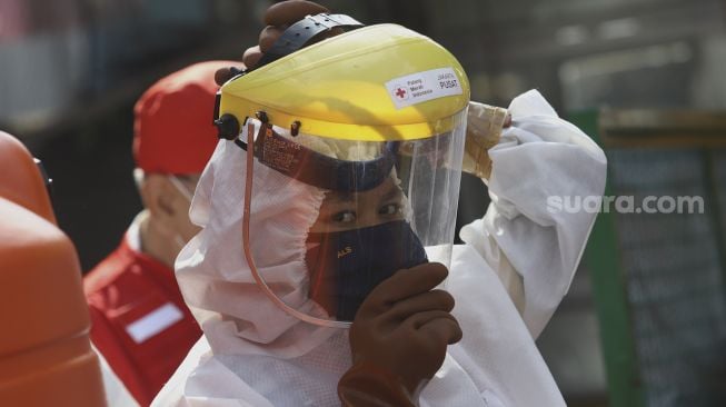 Petugas Palang Merah Indonesia (PMI) memakai penutup wajah bersiap menyemprotkan cairan disinfektan di lingkungan asrama Sekolah Tinggi Teknologi (STT) Bethel di kawasan Petamburan, Jakarta, Jumat (17/4).  [Suara.com/Angga Budhiyanto]