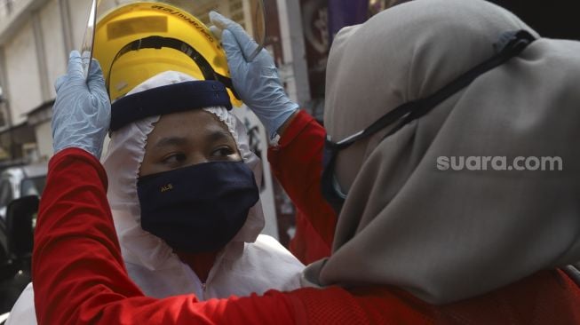 Petugas Palang Merah Indonesia (PMI) memakai helm bersiap menyemprotkan cairan disinfektan di lingkungan asrama Sekolah Tinggi Teknologi (STT) Bethel di kawasan Petamburan, Jakarta, Jumat (17/4).  [Suara.com/Angga Budhiyanto]