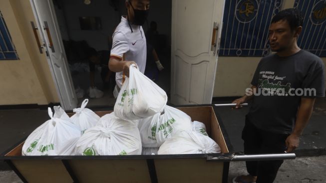 Pengurus membagikan paket bahan pangan kepada warga di kawasan Petamburan, Jakarta, Jumat (17/4). [Suara.com/Angga Budhiyanto]
