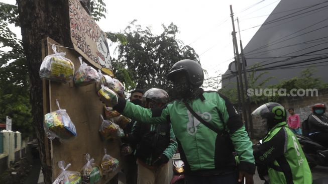 Pengemudi ojek online mengambil paket bahan makanan yang digantung oleh seniman wayang uwuh Iskandar Hardjodimuljo di salah satu pohon kawasan jalan Cawang Baru Utara, Jakarta Timur, Sabtu (18/4). [Suara.com/Angga Budhiyanto]