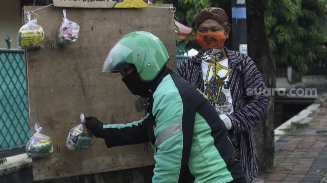 Pengemudi ojek online mengambil paket bahan makanan yang digantung oleh seniman wayang uwuh Iskandar Hardjodimuljo di salah satu pohon kawasan jalan Cawang Baru Utara, Jakarta Timur, Sabtu (18/4). [Suara.com/Angga Budhiyanto]