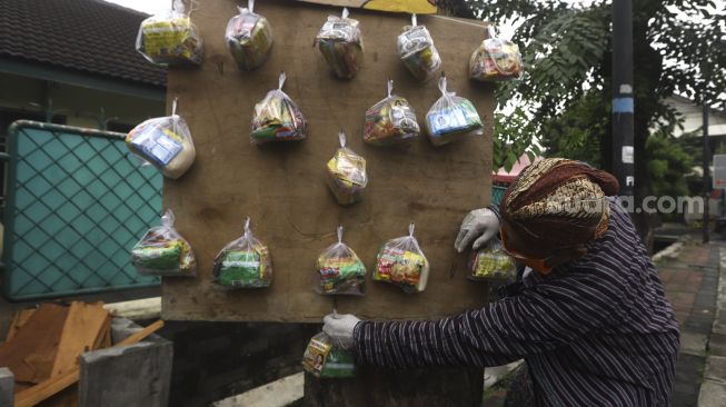 Seniman wayang uwuh Iskandar Hardjodimuljo menggantungkan sumbangan paket bahan makanan di salah satu pohon kawasan jalan Cawang Baru Utara, Jakarta Timur, Sabtu (18/4). [Suara.com/Angga Budhiyanto]