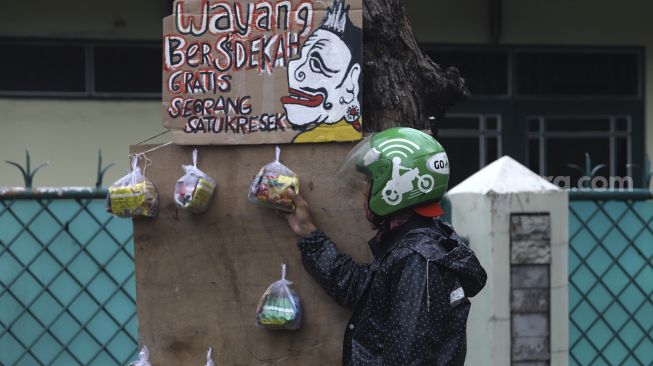 Pengemudi ojek online mengambil paket bahan makanan yang digantung oleh seniman wayang uwuh Iskandar Hardjodimuljo di salah satu pohon kawasan jalan Cawang Baru Utara, Jakarta Timur, Sabtu (18/4). [Suara.com/Angga Budhiyanto]