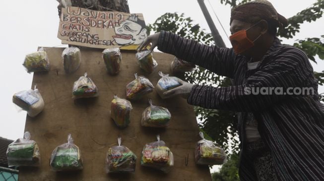 Seniman wayang uwuh Iskandar Hardjodimuljo menggantungkan sumbangan paket bahan makanan di salah satu pohon kawasan jalan Cawang Baru Utara, Jakarta Timur, Sabtu (18/4). [Suara.com/Angga Budhiyanto]