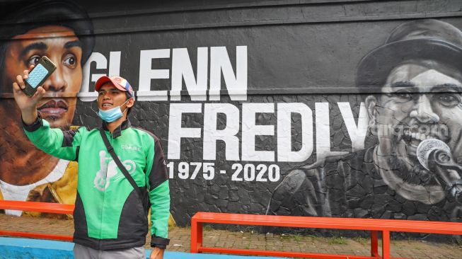 Warga berfoto di depan mural bergambar musisi Glenn Fredly  di Lapangan Basket Panglima Polim, Jakarta Selatan, Selasa (21/4). .[Suara.com/Alfian Winanto]
