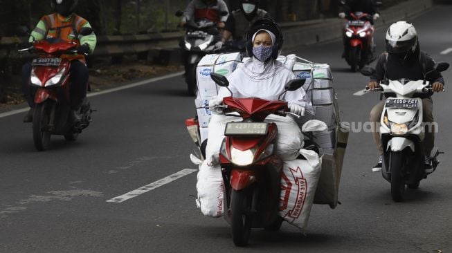 Seorang perempuan membawa barang dengan menggunakan motor melintas di Jalan TB Simatupang, Jakarta, Selasa (21/4). [Suara.com/Angga Budhiyanto]