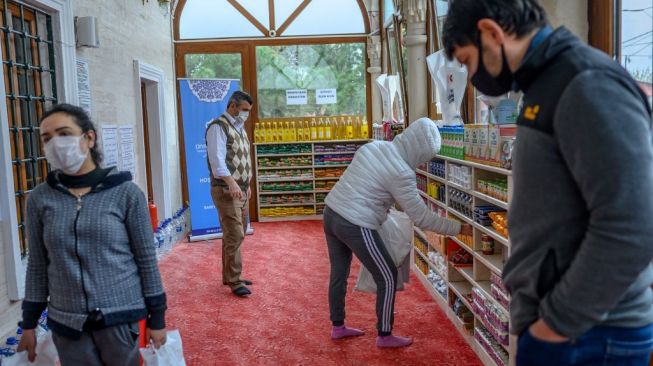 Sejumlah orang mengambil barang kebutuhan pokok di tempat yang dahulunya jadi rak sepatu di Masjid Dedeman, Turki, Selasa (21/4/2020). [AFP/Bulent Kilic]