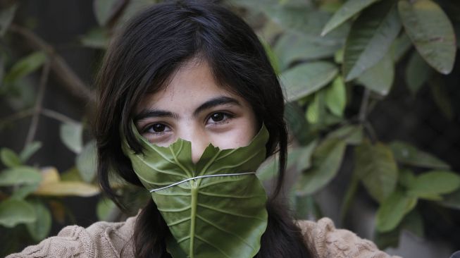 Seorang anak berpose dengan masker yang terbuat dari daun kubis ditengah wabah virus Corona, di Beit Lahia, Jalur Gaza, Palestina, Kamis (16/4/2020).  (AFP/Mohamed Abed)