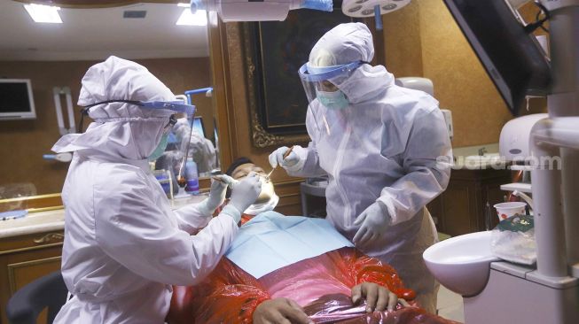 Tim dokter menggunakan alat perlindungan diri (APD) bersiap melakukan pemeriksaan gigi di salah satu klinik di kawasan Pulo Gadung, Jakarta, Rabu (22/4).  [Suara.com/Angga Budhiyanto]