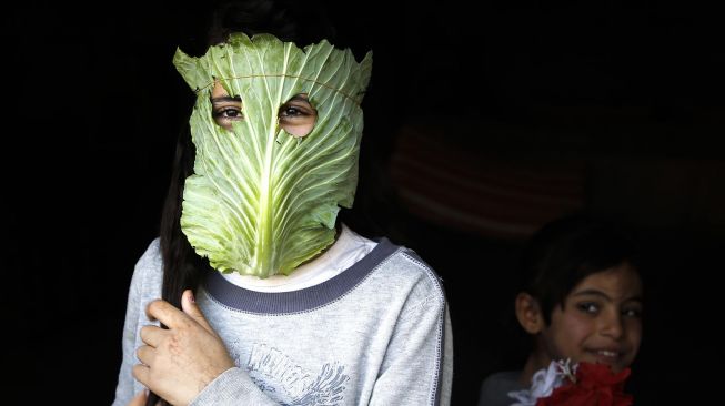 Seorang anak memakai masker dari daun kubis di Beit Lahia, Jalur Gaza, Palestina, Kamis (16/4/2020).  (AFP/Mohamed Abed)