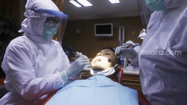 Tim dokter menggunakan alat perlindungan diri (APD) melakukan pemeriksaan gigi seorang pasien di salah satu klinik di kawasan Pulo Gadung, Jakarta, Rabu (22/4). [Suara.com/Angga Budhiyanto]